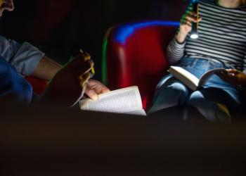 Das Foto zeigt zwei Personen, die im Dunklen mit Hilfe von Taschenlampen lesen