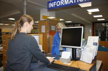 Eine Mitarbeiterin der Stadtbücherei steht an der Information und berät eine Frau bei der Anmeldung. 