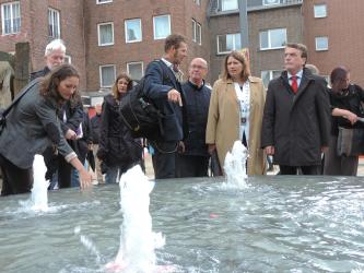 Brunnen im Vordergrund und die Bürgermeisterin mit mehrere Personen im Hintergrund 