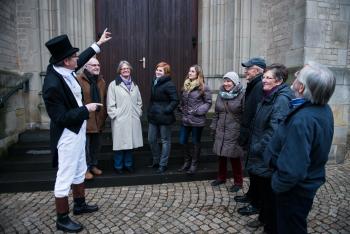 Ein Stadtführer erklärt einer Besucher*innen-Gruppe vor dem Willibrordi-Dom den Eingangsbereich des historischen Gebäudes.