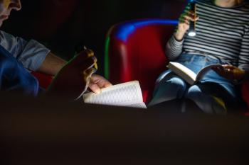 Das Foto zeigt zwei Personen, die im Dunklen mit Hilfe von Taschenlampen lesen